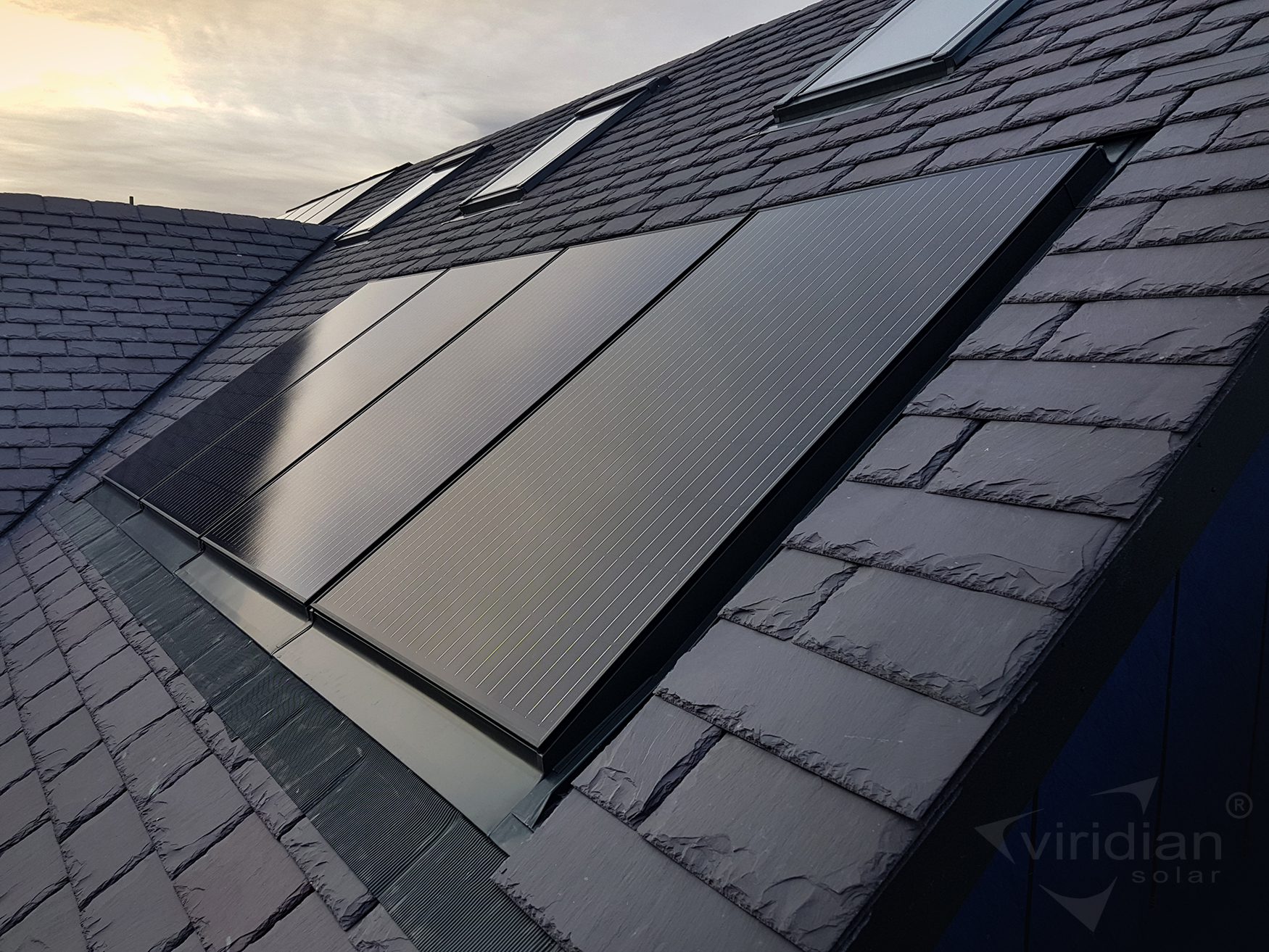 3045-slate-roof-integrated-solar-PV-Ecolek(C)ViridianSolar Rooftop solar panels installed on a slate-tiled roof under a cloudy sky.